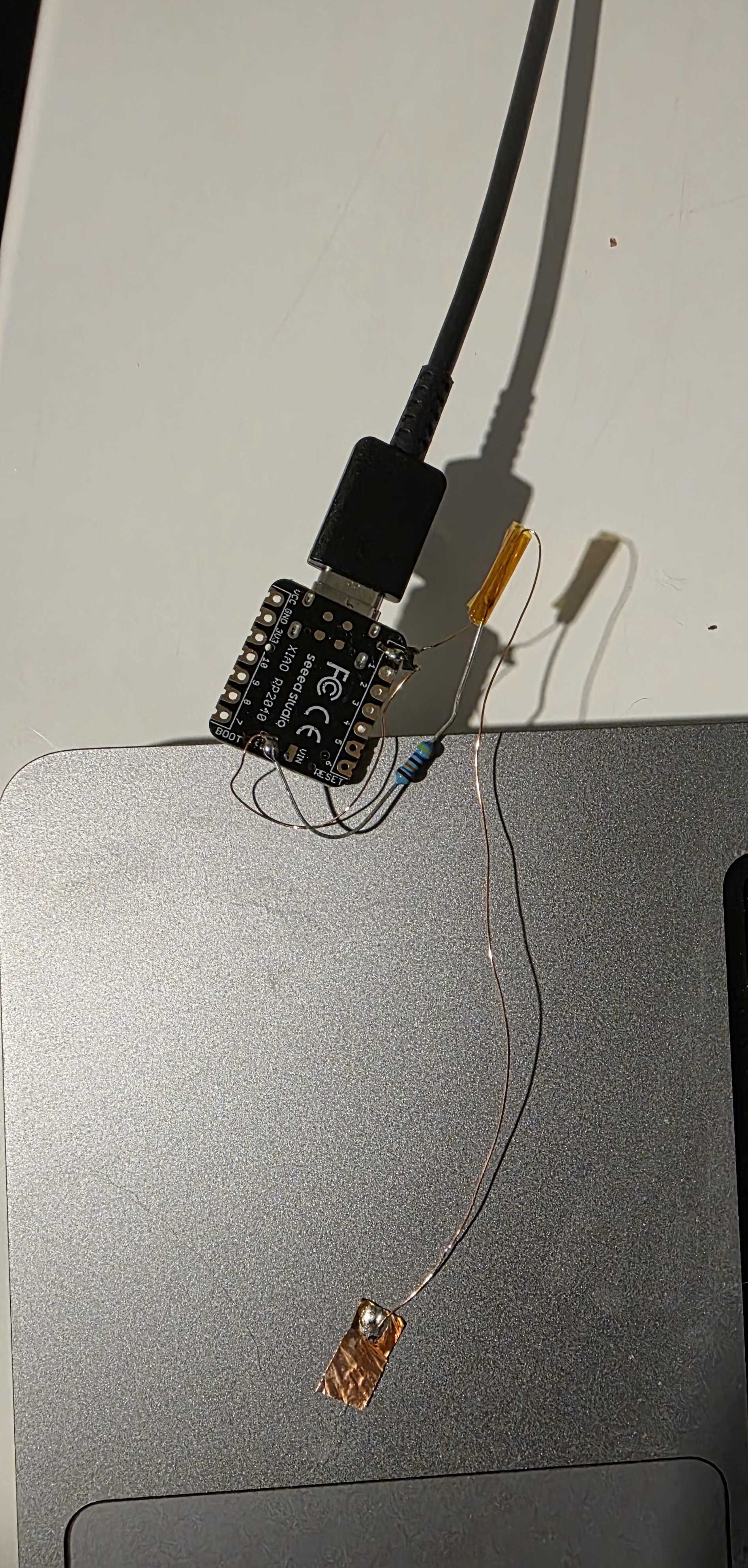 Seeed XIAO RP2040 microcontroller with a resistor and a thin wire leading to a copper foil contact pad.